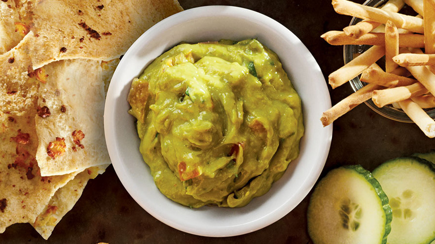 Guacamole with Dorothy Lynch Home Style Recipe in a white bowl with tortilla chips and cucumbers beside