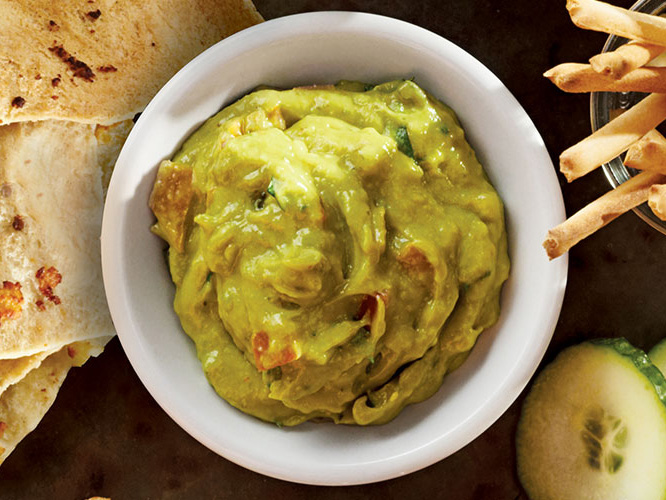 Guacamole with Dorothy Lynch Home Style Recipe in a white bowl with tortilla chips and cucumbers beside