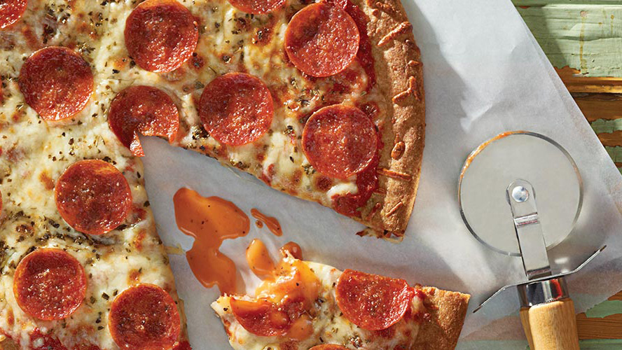 Dottie Lynch’s Home Style Pizza on parchment paper with a pizza cutter laying next to it