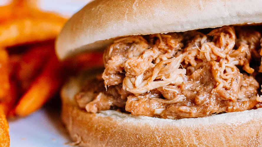 BBQ Pulled Chicken Sandwich with sweet potato fries in the background