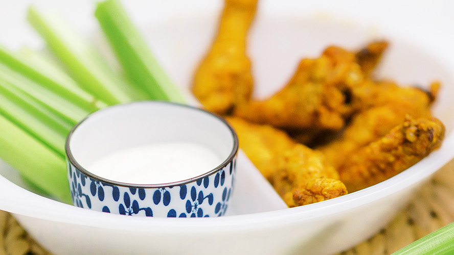 Air Fryer Buffalo Wings in a white bowl, a blue and white ramekin with ranch, and some celery, only the ranch bowl is in focus