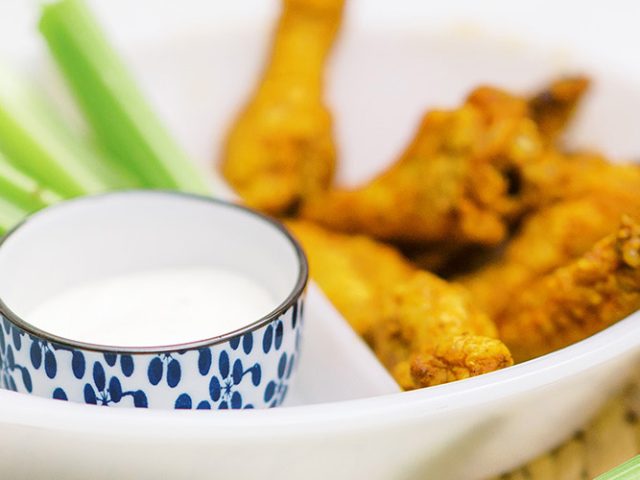 Air Fryer Buffalo Wings in a white bowl, a blue and white ramekin with ranch, and some celery, only the ranch bowl is in focus
