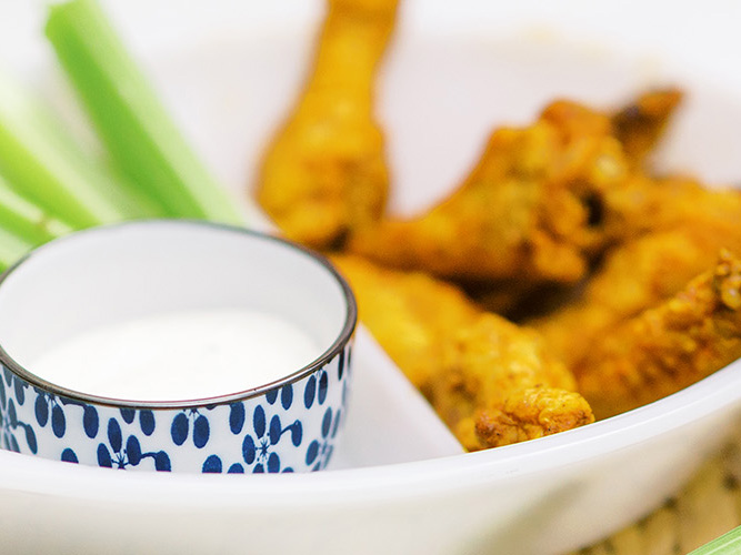 Air Fryer Buffalo Wings in a white bowl, a blue and white ramekin with ranch, and some celery, only the ranch bowl is in focus