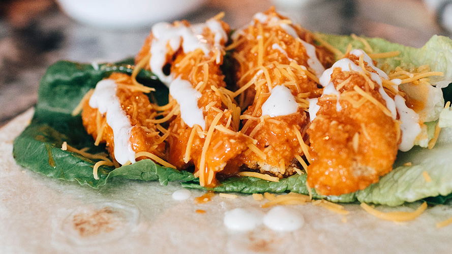 Tortilla with lettuce and four chicken strips on top drizzled with buffalo sauce, Dorothy Lynch, ranch, and cheese- taco is unwrapped