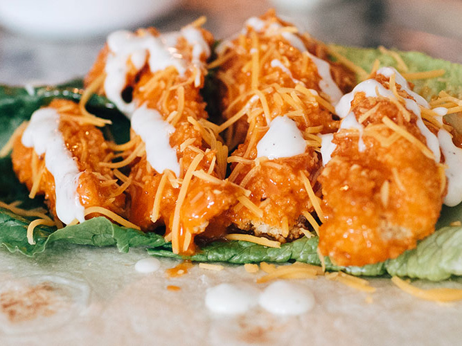 Tortilla with lettuce and four chicken strips on top drizzled with buffalo sauce, Dorothy Lynch, ranch, and cheese- taco is unwrapped