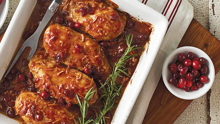 Dorothy Lynch Cranberry Chicken in a white pan with some rosemary for garnish as well as a side bowl of cranberries