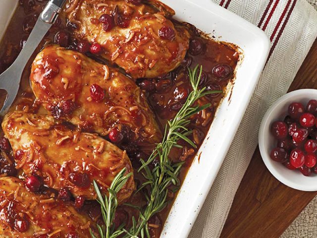 Dorothy Lynch Cranberry Chicken in a white pan with some rosemary for garnish as well as a side bowl of cranberries
