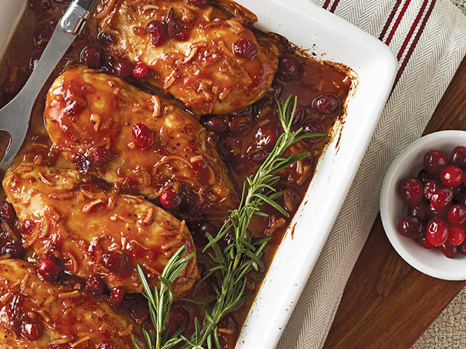 Dorothy Lynch Cranberry Chicken in a white pan with some rosemary for garnish as well as a side bowl of cranberries