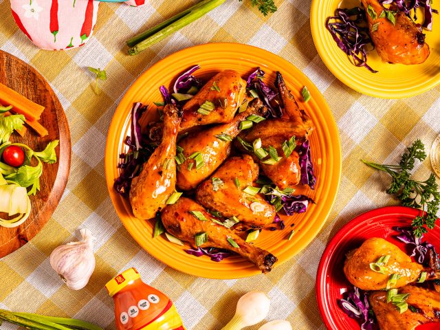 Dorothy Lynch Barbecue Chicken Wings on centered on an orange plate. Smaller plates surrounding larger plate with more wings. Yellow checkered table cloth under everything.
