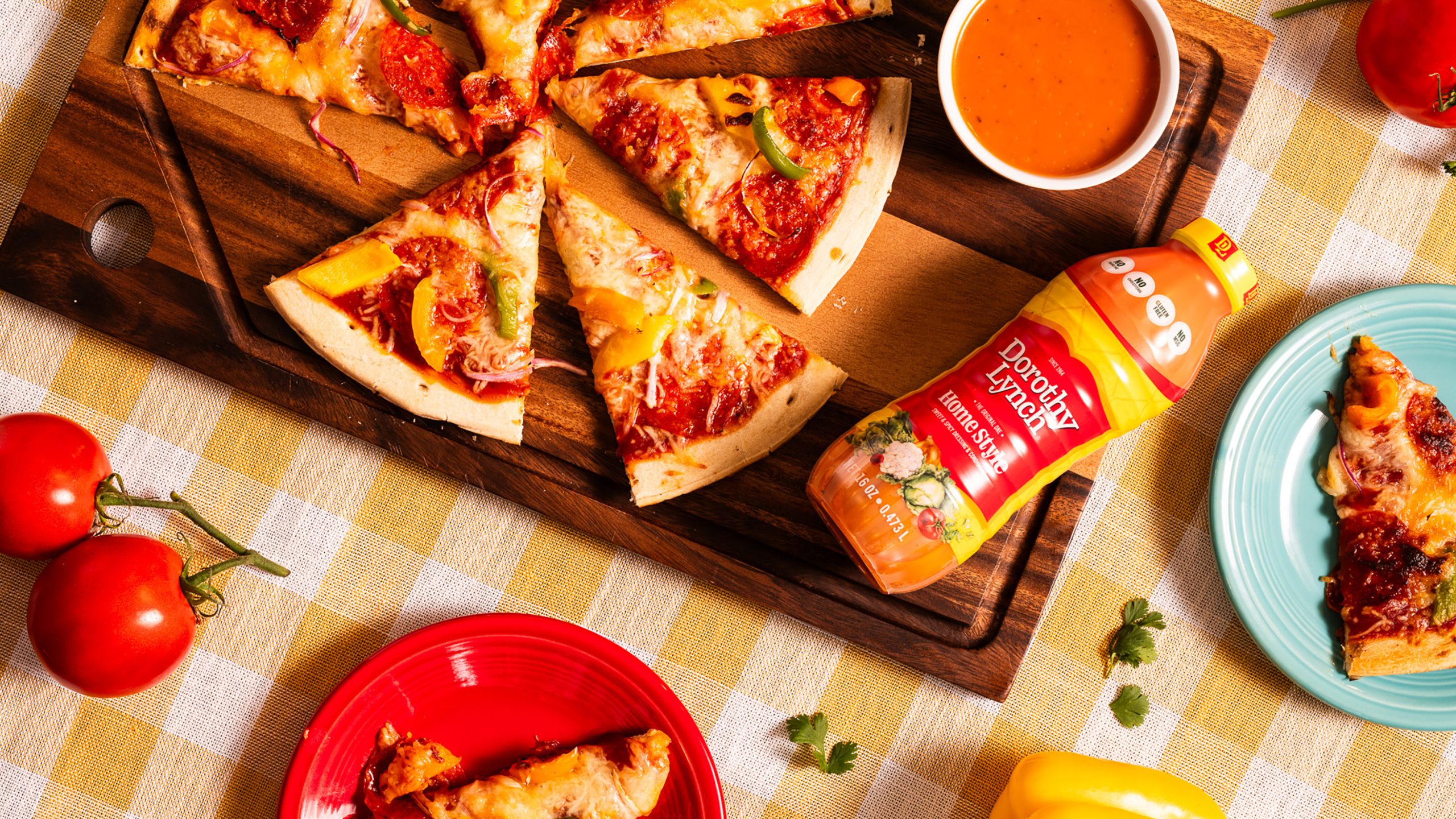 Dorothy Lynch Pizza and Dipping Sauce on a wooden board. checkered table cloth underneath, fun colored plates with pieces of pizza scattered