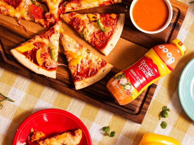 Dorothy Lynch Pizza and Dipping Sauce on a wooden board. checkered table cloth underneath, fun colored plates with pieces of pizza scattered