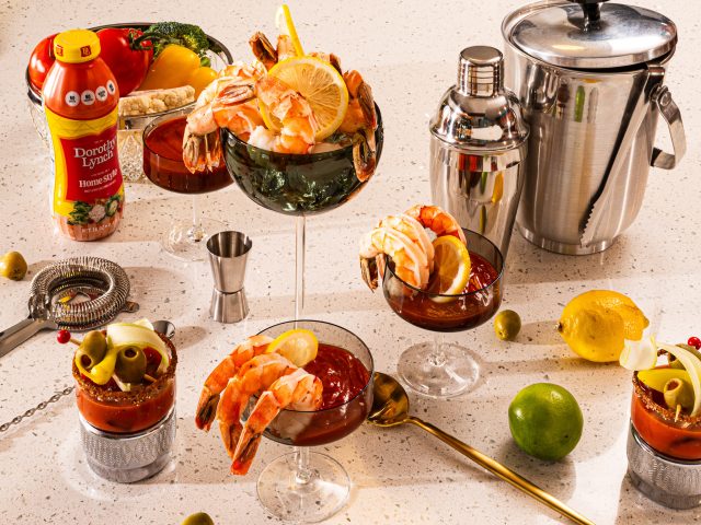 Dorothy Lynch Dressing Shrimp Cocktail Sauce in fancy glass with lots of cocktail equipment , veggies, and Dorothy Lynch Dressing scattered around