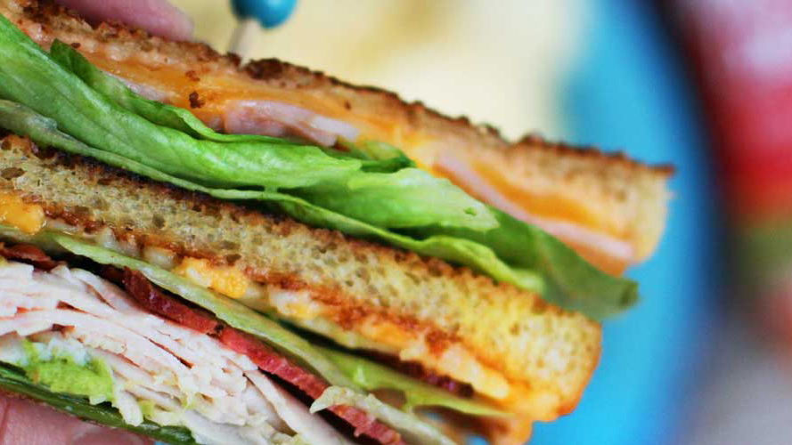 Side cross section view of a Grilled Club sandwich with lettuce, deli meat, and Dorothy Lynch