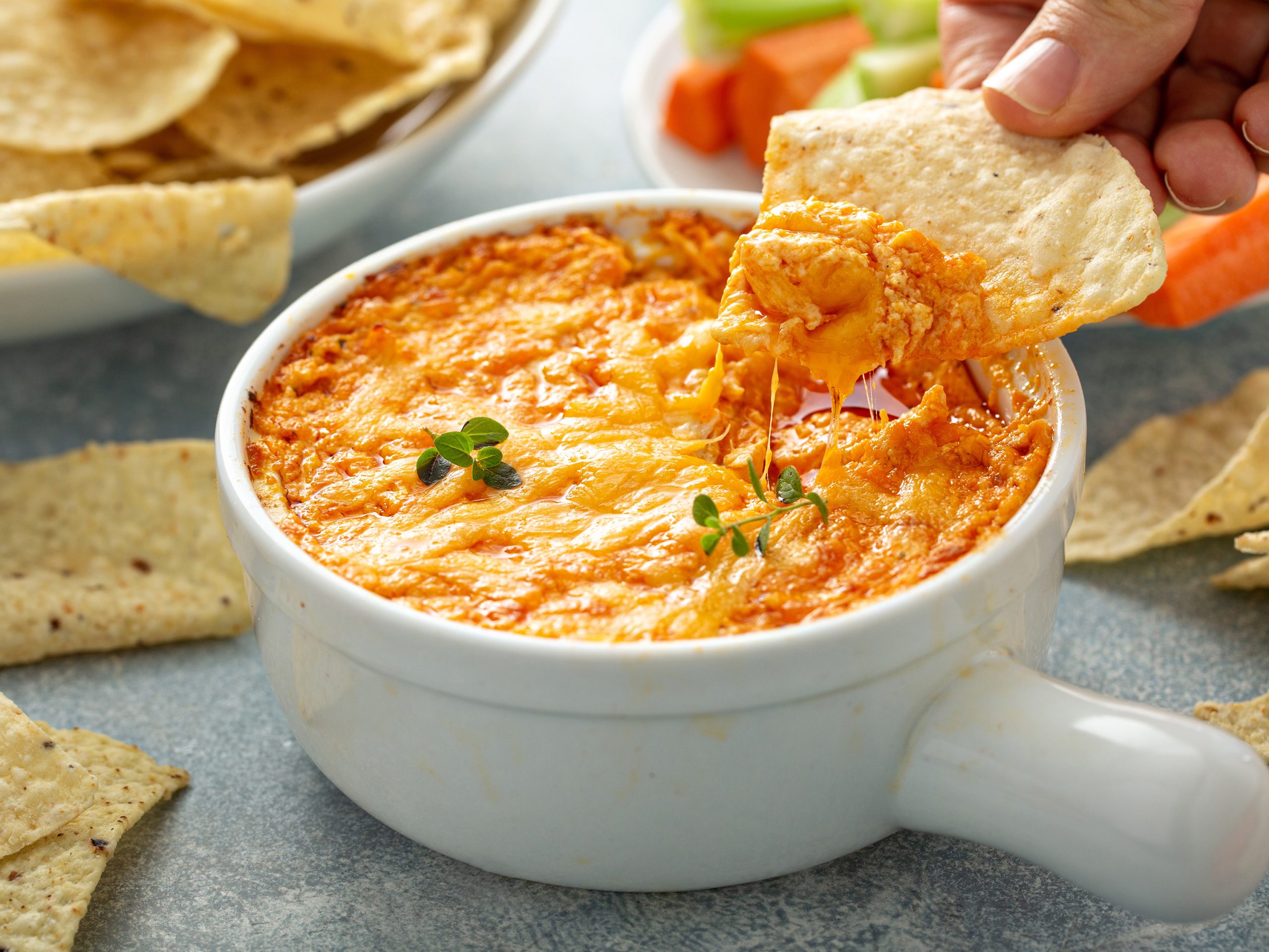 Dorothy Lynch Cheesy Buffalo Chicken Dip Recipe with someone actively dipping a chip into the dip