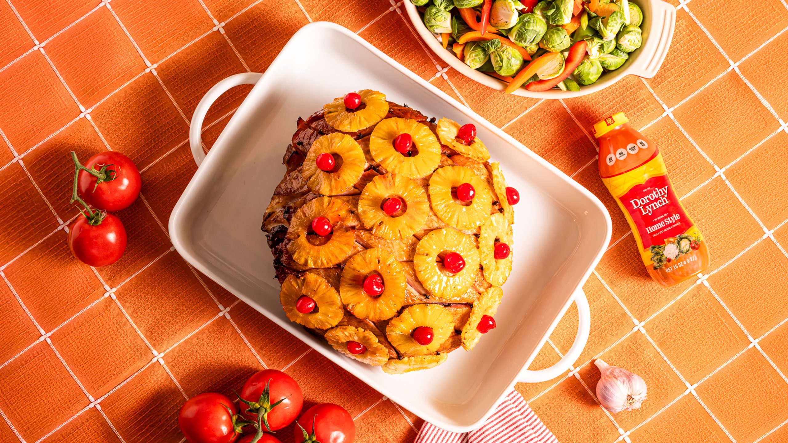 Glazed Ham in white Baking dish with pineapple rings and other decor anointed on top of the ham. All sitting on an orange table cloth