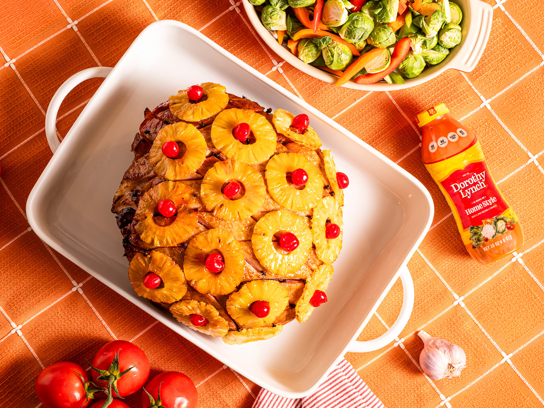Glazed Ham in white Baking dish with pineapple rings and other decor anointed on top of the ham. All sitting on an orange table cloth