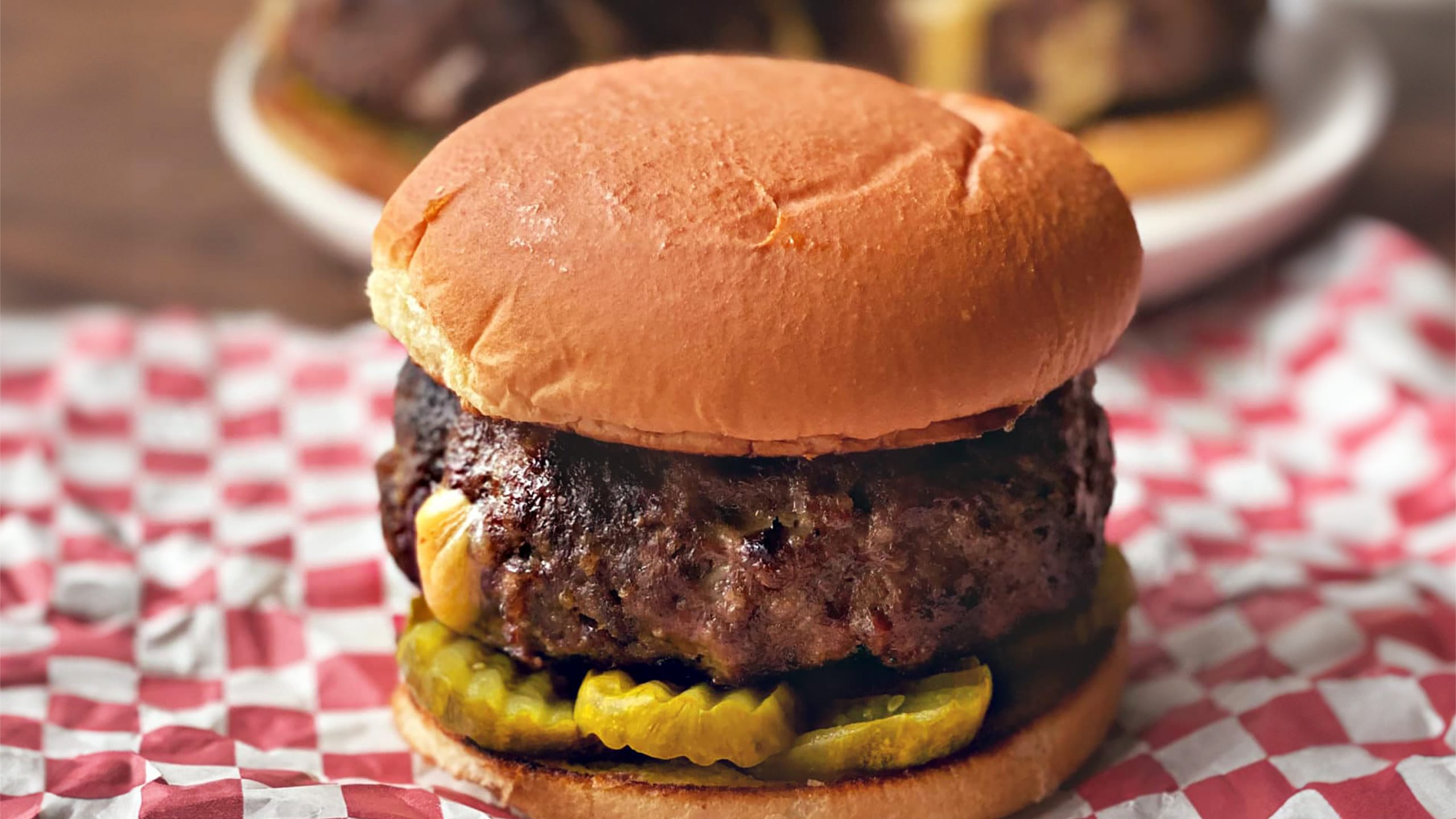 Juicy Lucy Burger, with bun and pickles, sitting on red checkered parchment paper