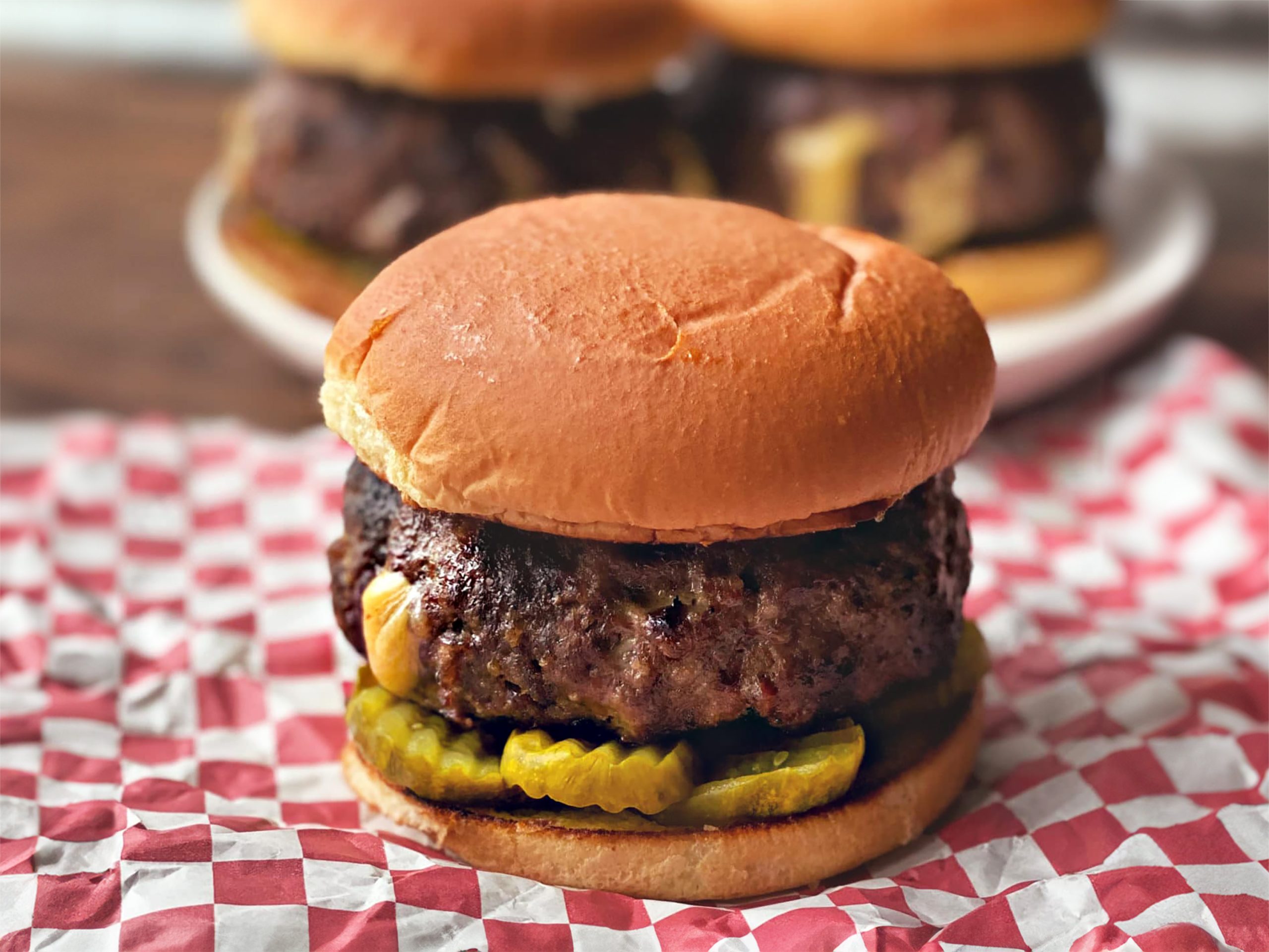 Juicy Lucy Burger, with bun and pickles, sitting on red checkered parchment paper