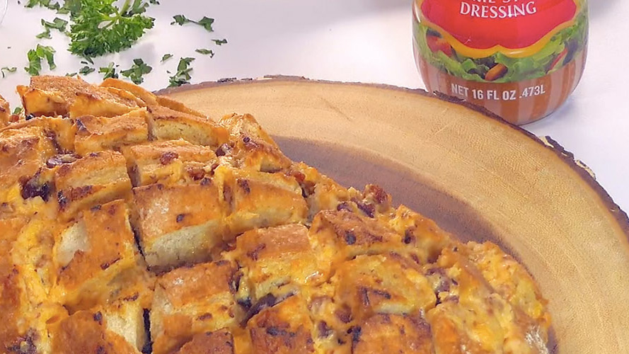 Dorothy’s Cheesy Bacon Pull-Apart Bread on a wooden board with the bottom of a Dorothy Lynch bottle barely in frame (upper right corner)