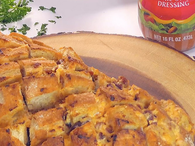 Dorothy’s Cheesy Bacon Pull-Apart Bread on a wooden board with the bottom of a Dorothy Lynch bottle barely in frame (upper right corner)