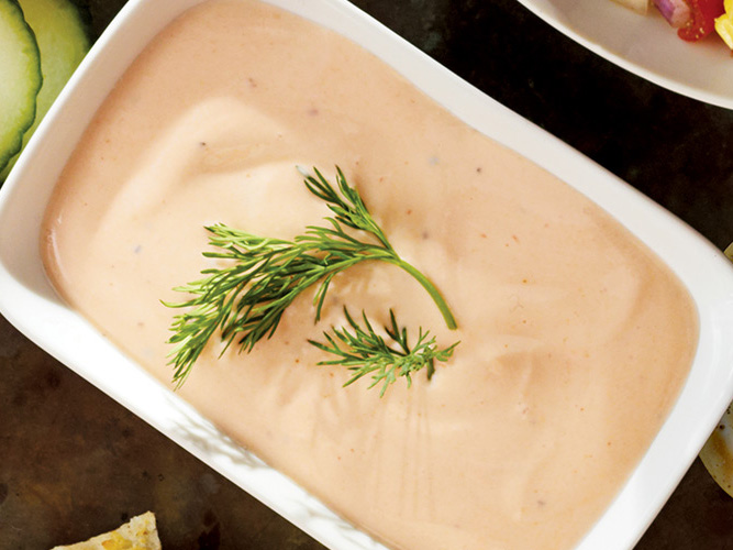 Dorothy’s Light & Lean Spicy Greek Dip in a white bowl with some sort of green herb laying on top of the dip adding color and decor