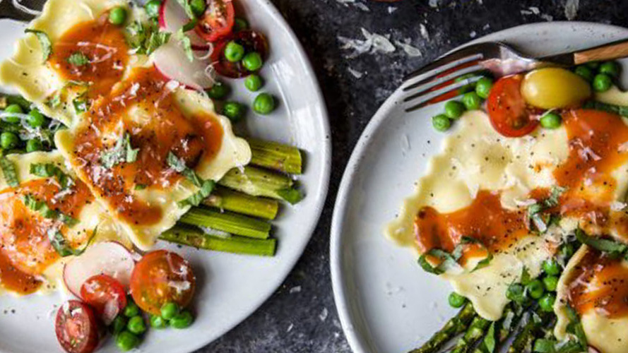Two white plates of Garden Veggie Ravioli With Smoky Dorothy Lynch Dressing with other cooked vegetables on the plates as well