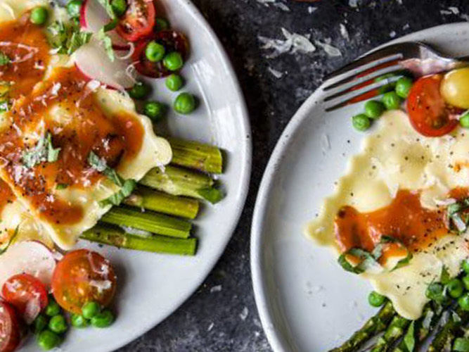 Two white plates of Garden Veggie Ravioli With Smoky Dorothy Lynch Dressing with other cooked vegetables on the plates as well